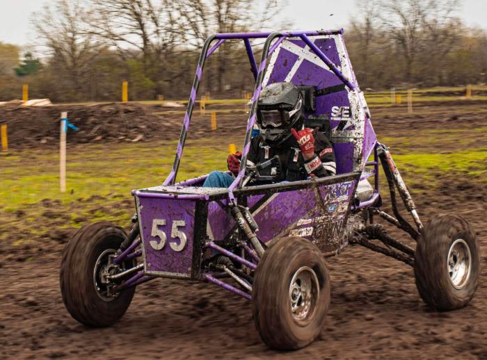 Person driving a purple Baja Sae vehicle on a mud race track. 