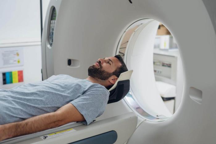 Man wearing a gray shirt laying on a bed entering an x-ray machine