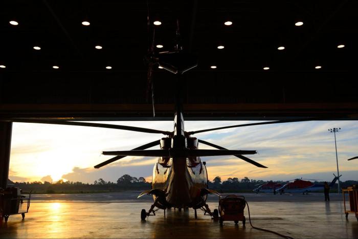 Back view of a helicopter on the ground in an open garage. There is a sunrise in front of the helicopter.